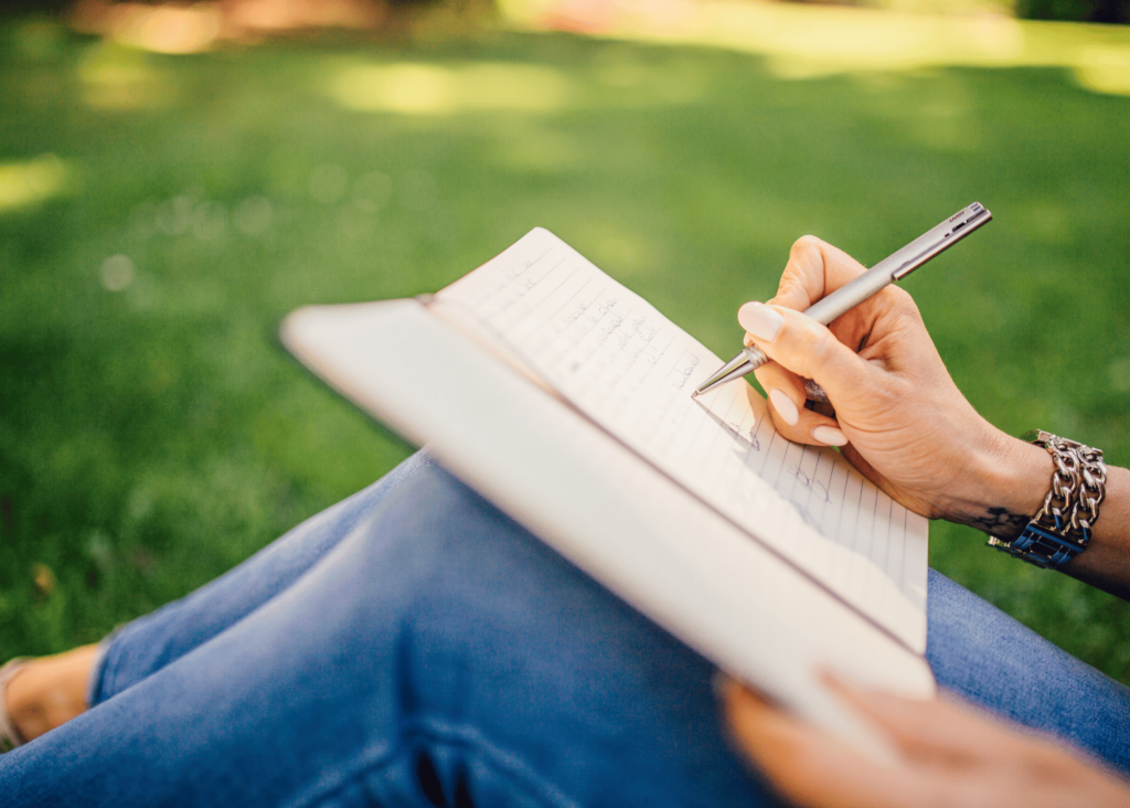 stock photo of a woman writing in a journal while seated in her yard